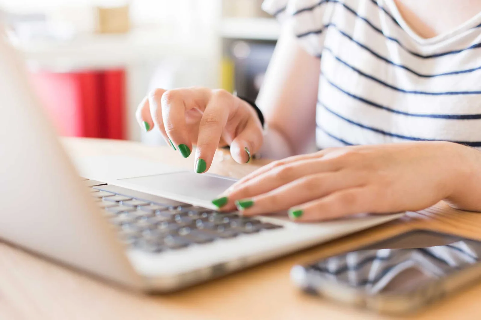 Hände mit grünen Nägeln tippen auf Laptop-Tastatur mit Monitor im Hintergrund