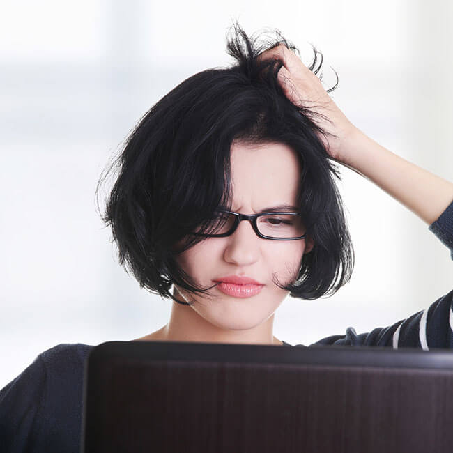 Junge Frau mit schwarzen Haaren und Brille rauft sich frustriert die Haare vor dem Laptop