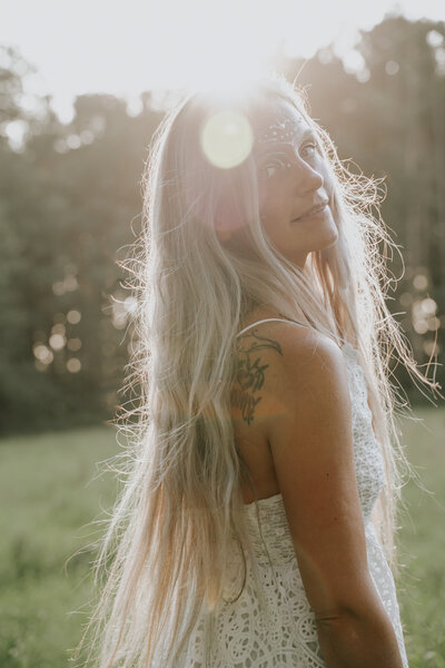 Blonde Frau mit Tattoo im Gegenlicht, mystische Waldatmosphäre, spirituelle Ausstrahlung