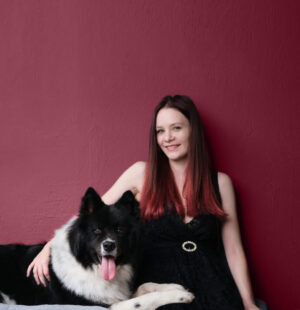 Frau mit schwarzem Hund vor burgunderfarbener Wand, Dog Dancing Kurs Autorin Alexandra Noll