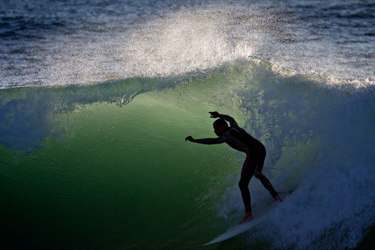 Surfer in Neoprenanzug auf Welle mit Gegenlicht