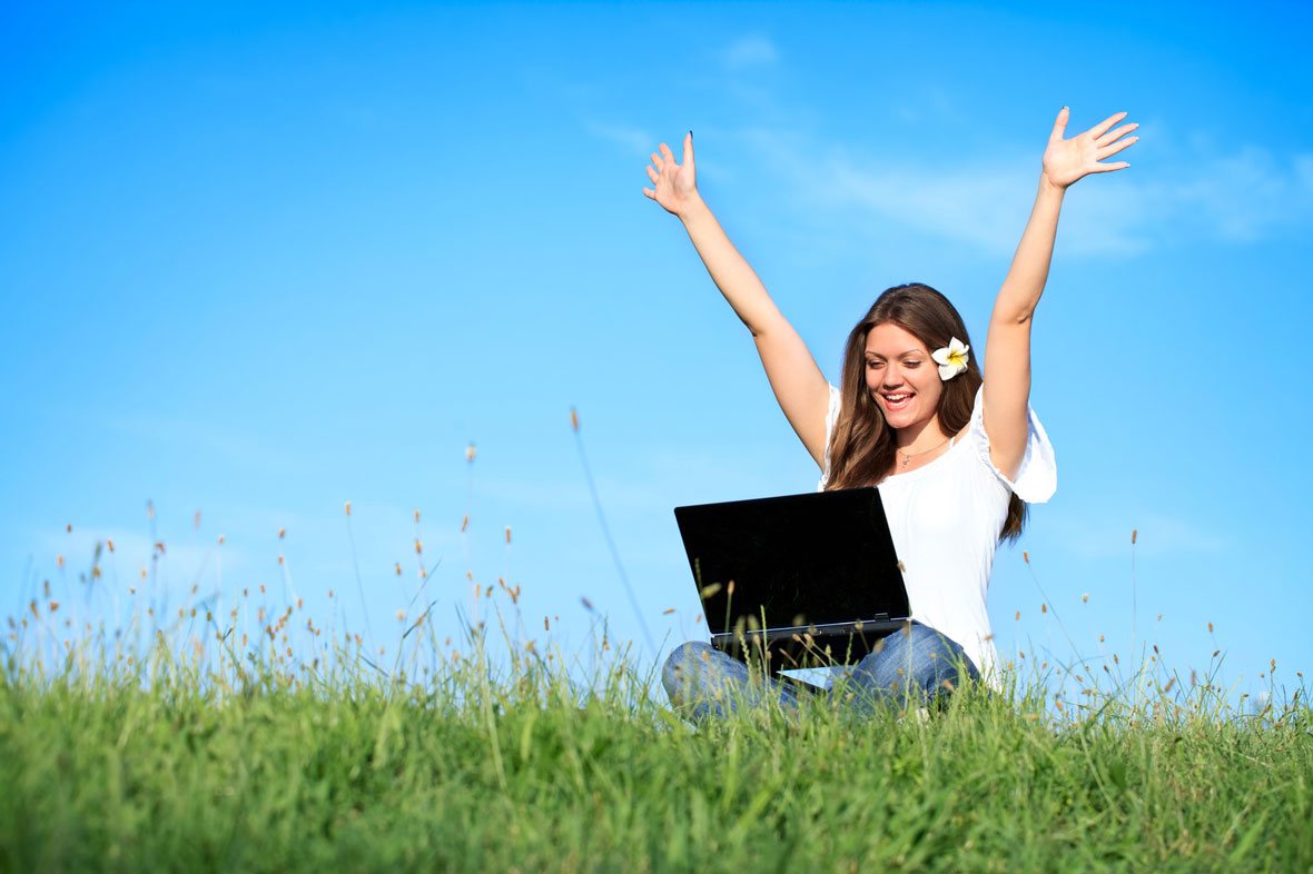 Frau mit Laptop auf Wiese unter blauem Himmel, Arme erhoben, weißes Shirt, weiße Blume im Haar – Symbolbild für digitale Radi