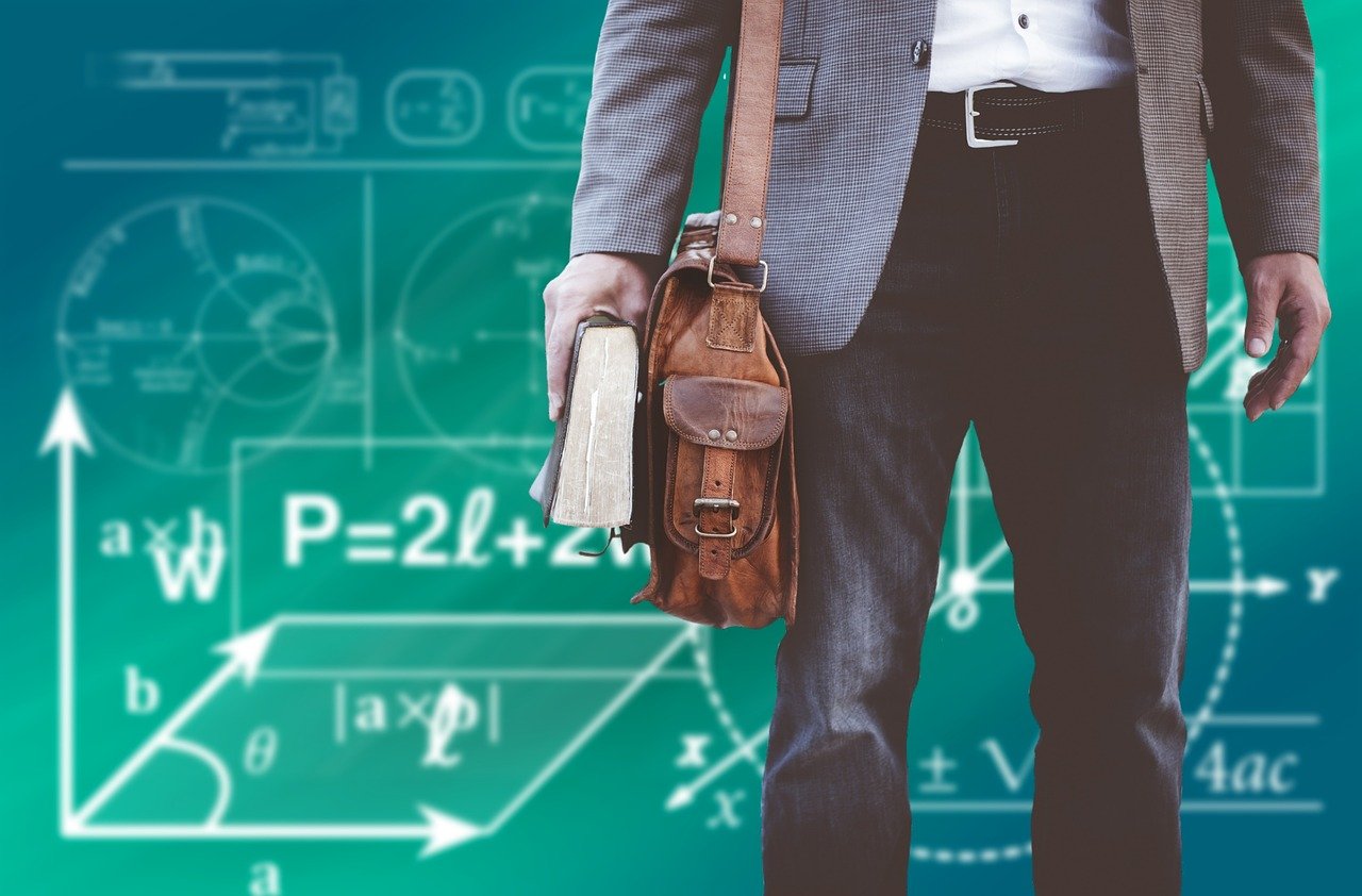 Lehrer in Anzug mit Tasche vor grüner Schultafel mit mathematischen Formeln, Symbolbild für Schulbildung