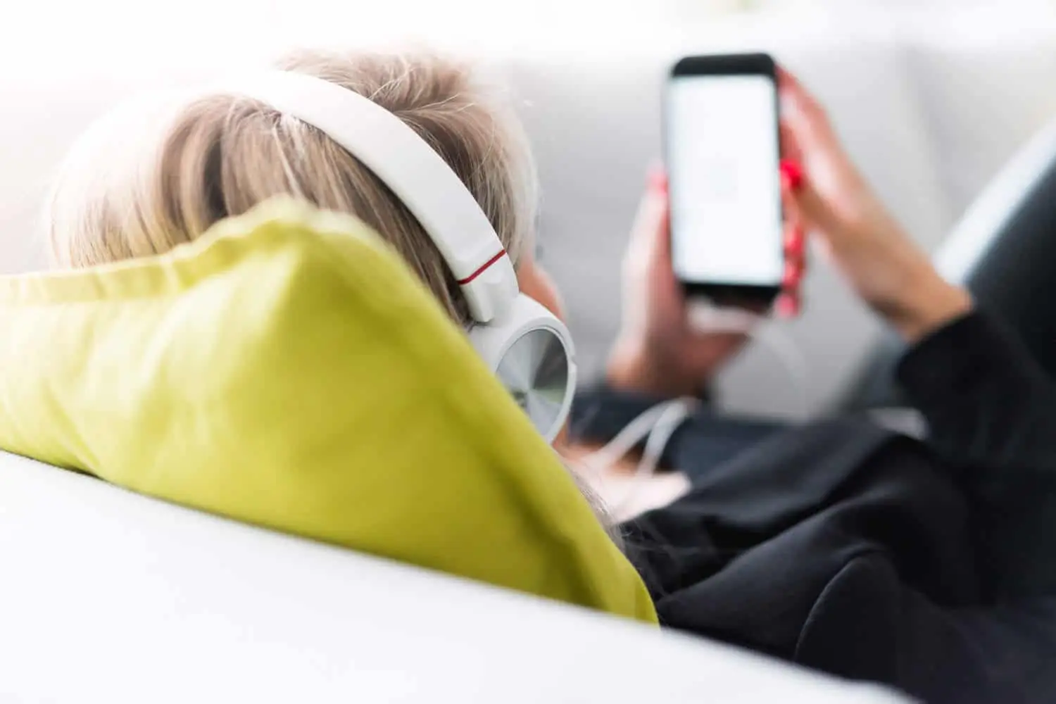 Frau mit Kopfhörern schaut auf Smartphone, Mann im Hintergrund mit Handy