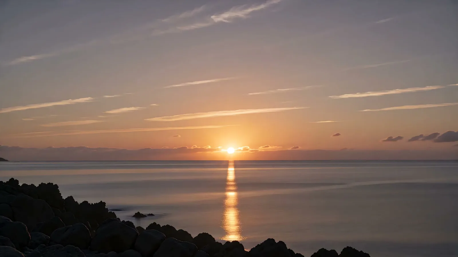 Sonnenaufgang über ruhiger See mit Lichtsäule und felsenreicher Küste