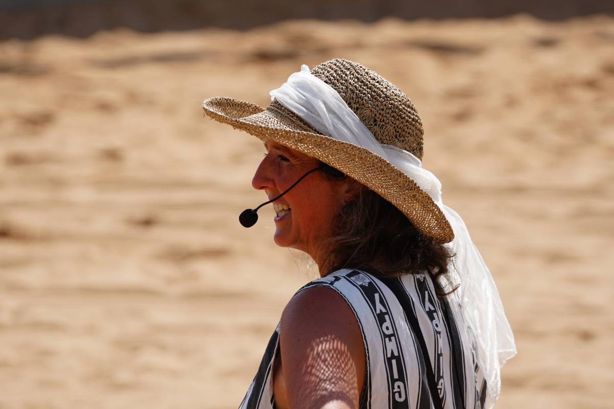 Christiane Göbel mit Headset-Mikrophone und Strohhut mit weißem Tuch vor Sandarena
