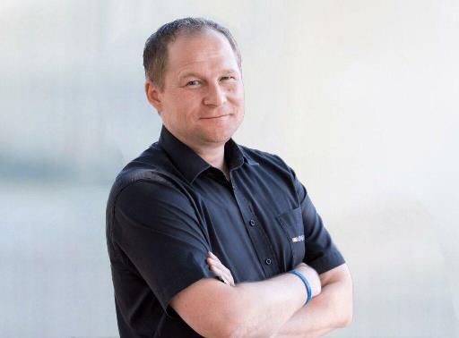 Einfach richtige Geldentscheidungen treffen! – Online-Finanzkurs 4 Klaus Rost in dunklem Hemd mit verschränkten Armen, seitliches Portrait vor Hintergrund