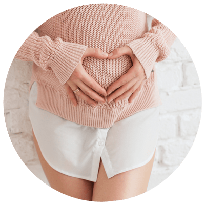 Schwangere Frau in rosa Pullover formt Herz mit Händen auf Bauch