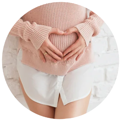 Schwangere Frau in rosa Pullover formt Herz mit Händen auf Bauch