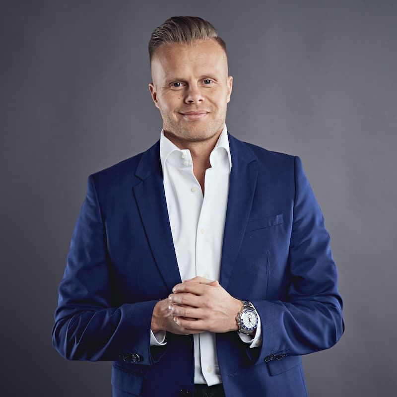 Gunnar Kessler, Autor des EIS Easy Income System Videokurses, in blauem Businessblazer und weißem Hemd vor grauem Hintergrund
