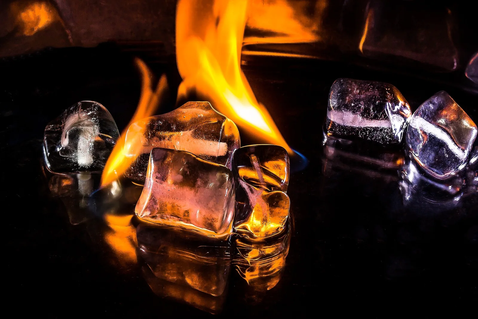 Gläser mit Whiskey und Eiswürfeln vor loderndem Feuer, dramatische Beleuchtung