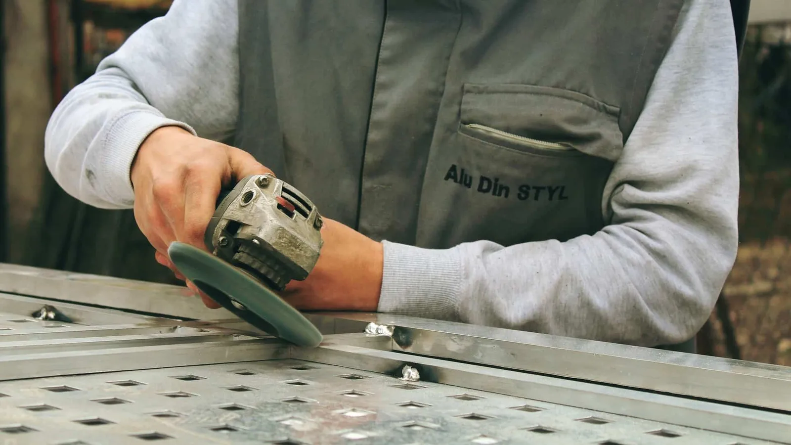Werkzeugmechaniker arbeitet mit Schleifwerkzeug an Metallplatte mit Bohrungen und Nut-Profilen
