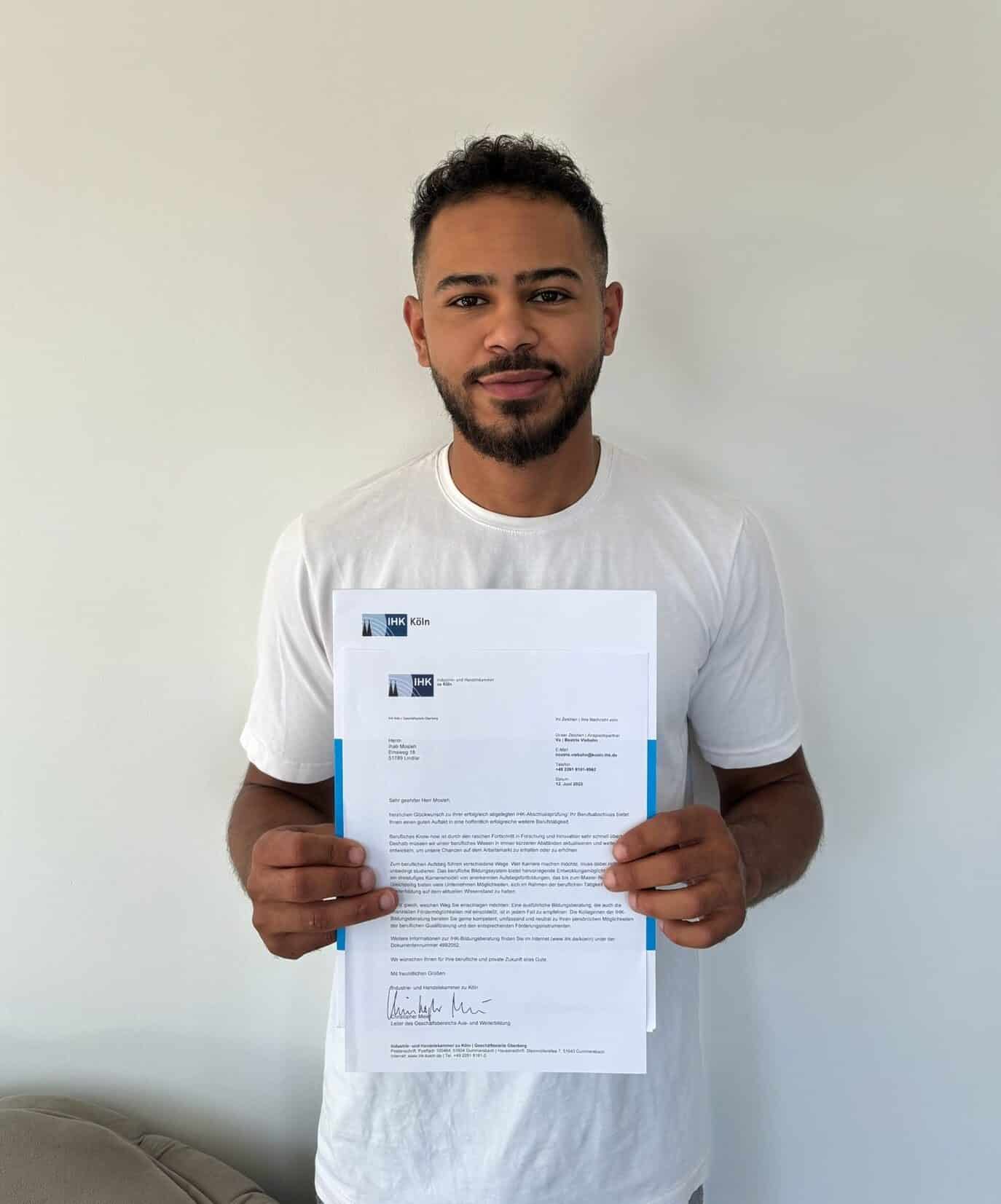 Ihab hält bestandenes IHK-Prüfungszertifikat in die Kamera