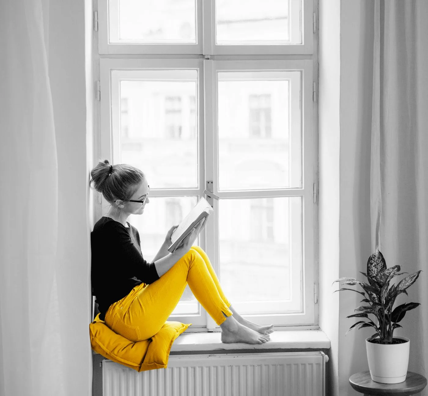 Farbfoto einer Frau im gelben Outfit auf Fensterbank lesend mit Pflanze, selektive Farbbearbeitung