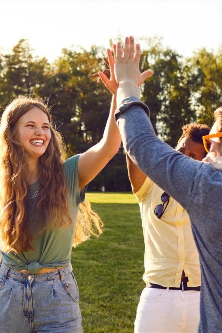 Gruppe lachender Menschen im Freien gibt sich High-Five bei Sonnenschein