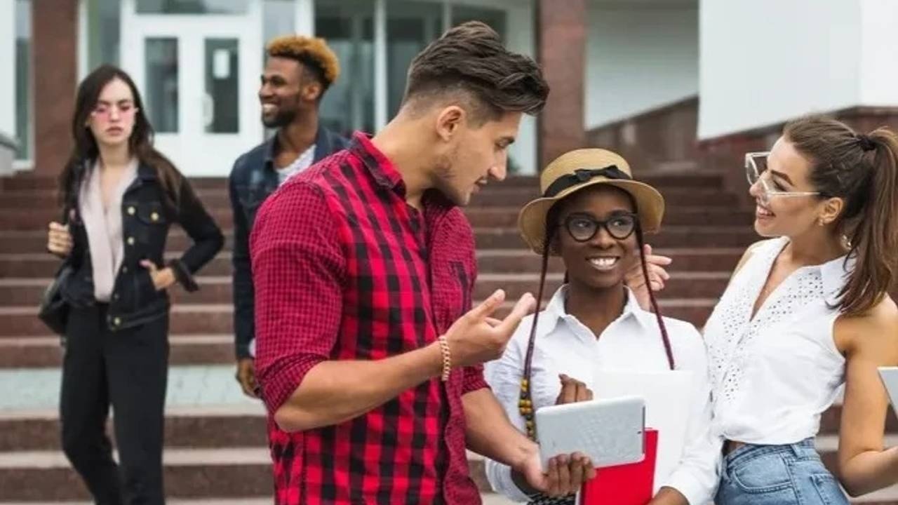 Junge Menschen auf Universitätsgelände halten Tablet und lachen zusammen