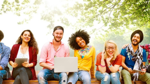 Diverse Gruppe lächelnder Menschen mit Tablet und Laptop unter grünen Bäumen sitzend