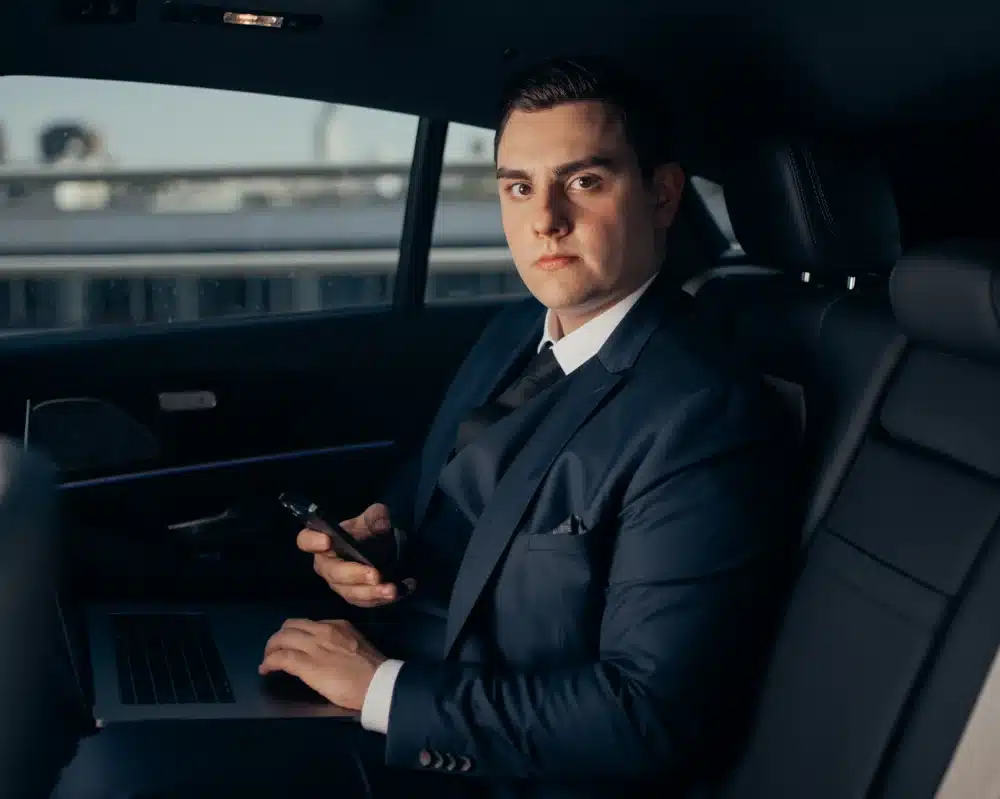 Testimonial-Foto eines Mannes im dunklen Anzug im Auto mit Handy