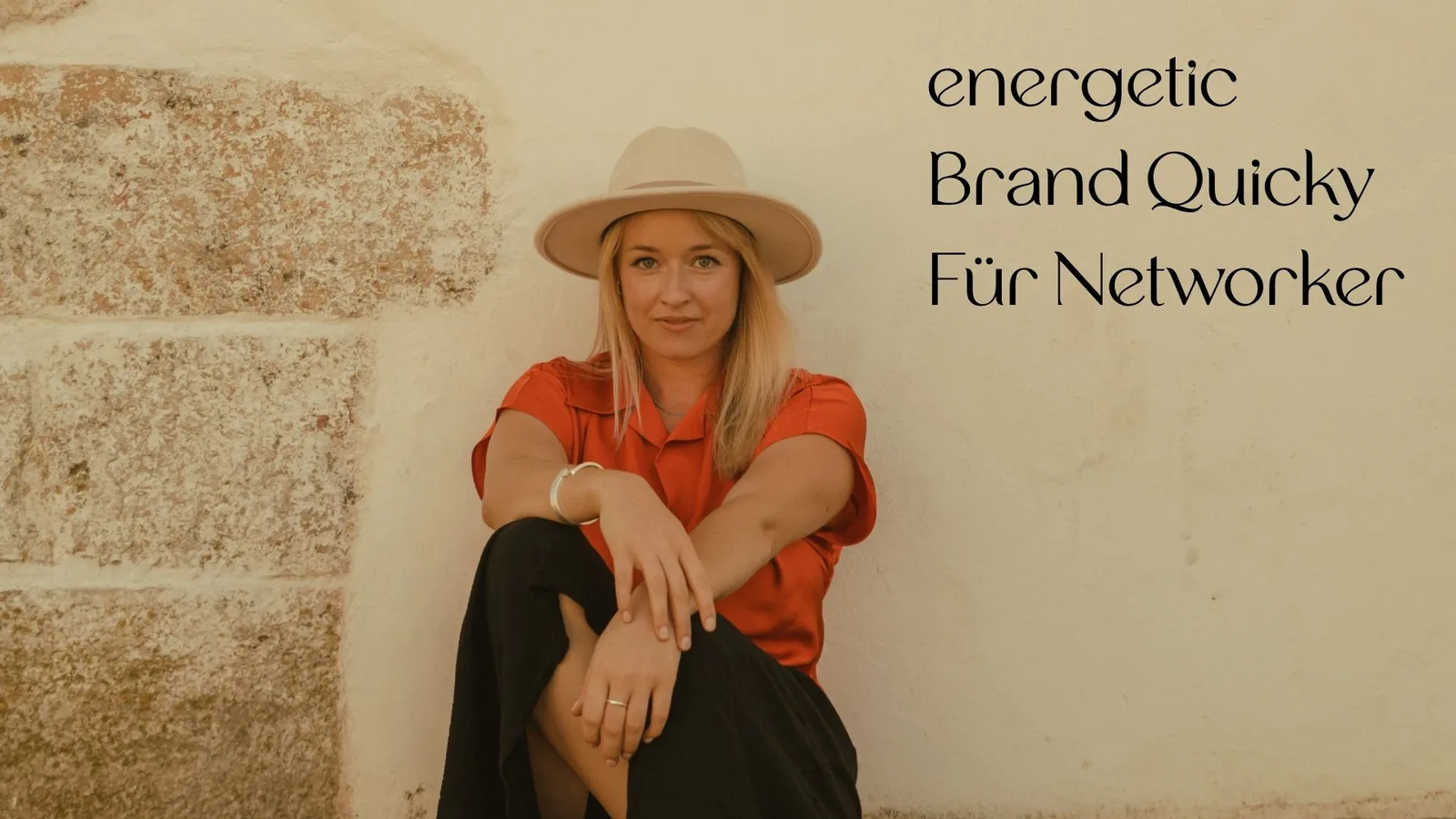 Frau in roter Bluse und Hut sitzt vor Backsteinwand – Energetic Brand Quicky für Networker