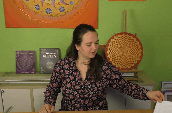Energiebilder selber malen – Online Videomalkurs Mandala 3 Frau in gemütlichem Setting vor grüner Wand mit Mandalas und Kunstbüchern