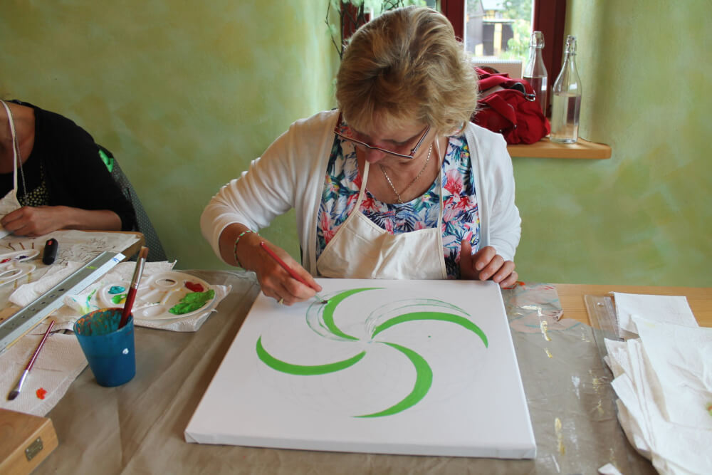 Energiebilder selber malen – Online Videomalkurs Mandala 17 Frau malt grüne geschwungene Linien als Mandala-Grundform auf weißem Papier