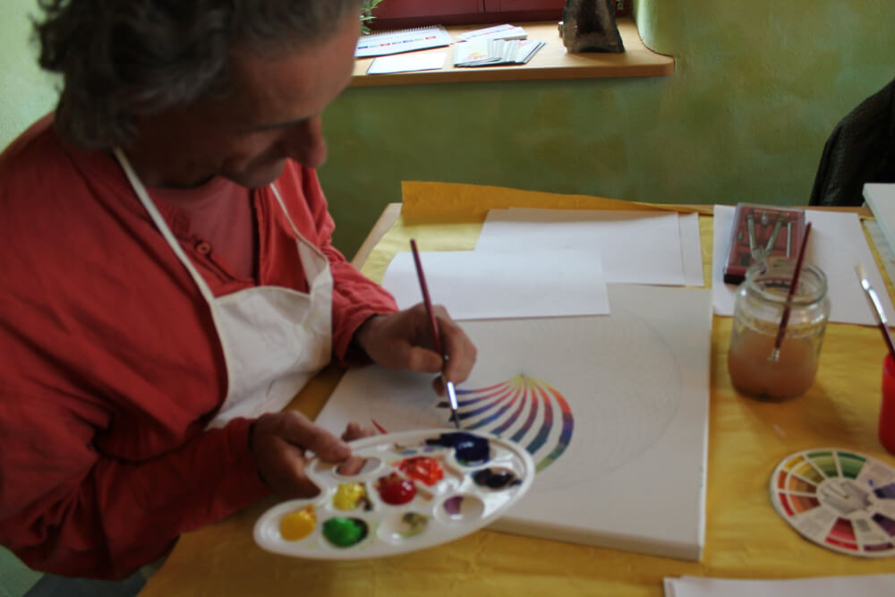 Energiebilder selber malen – Online Videomalkurs Mandala 18 Person malt mit Pinseln ein buntes Mandala mit Regenbogenfarben und Farbpalette