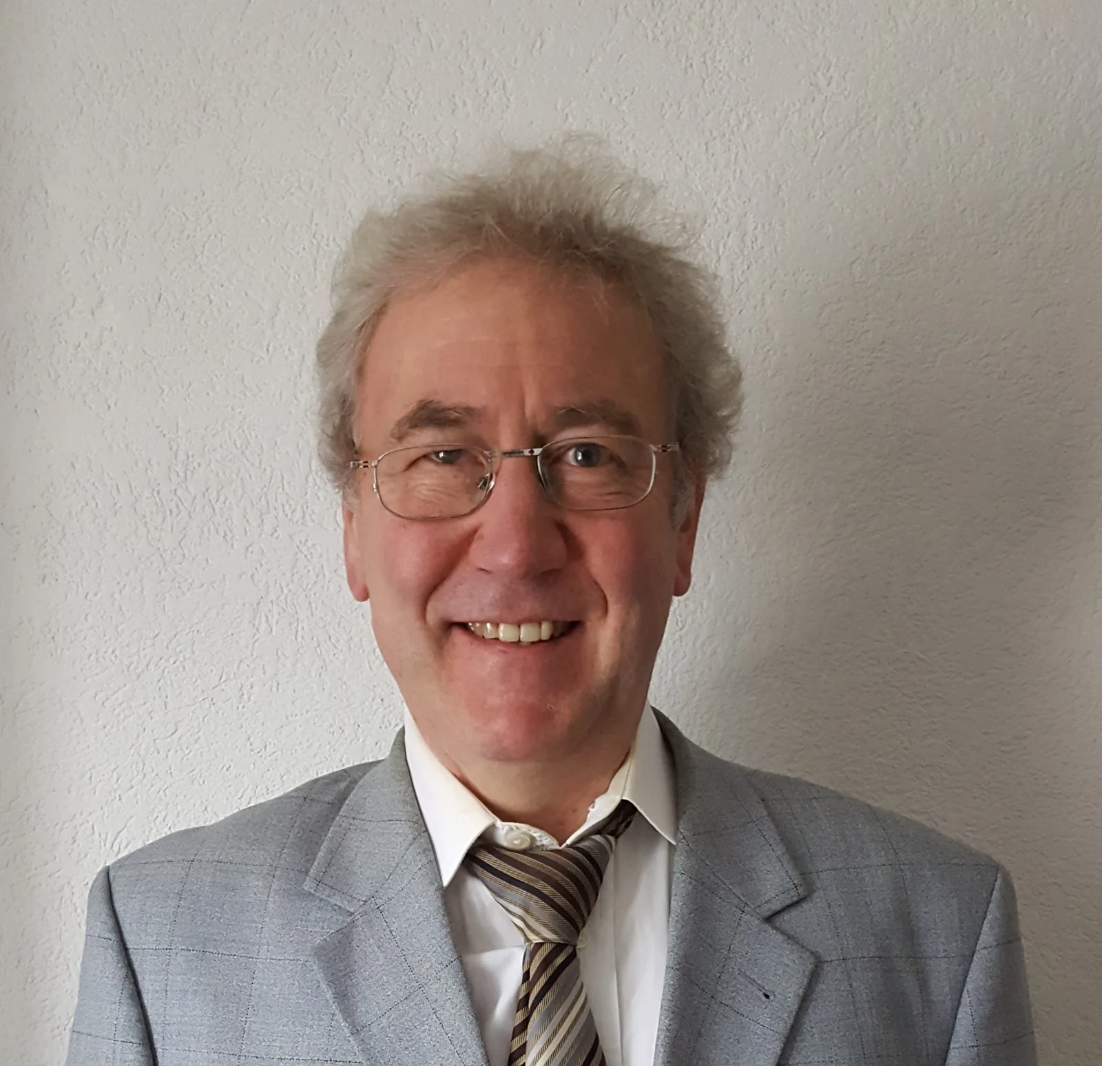 Porträt von Dr. Volker Schmiedel mit Brille im grauen Anzug und gestreifter Krawatte