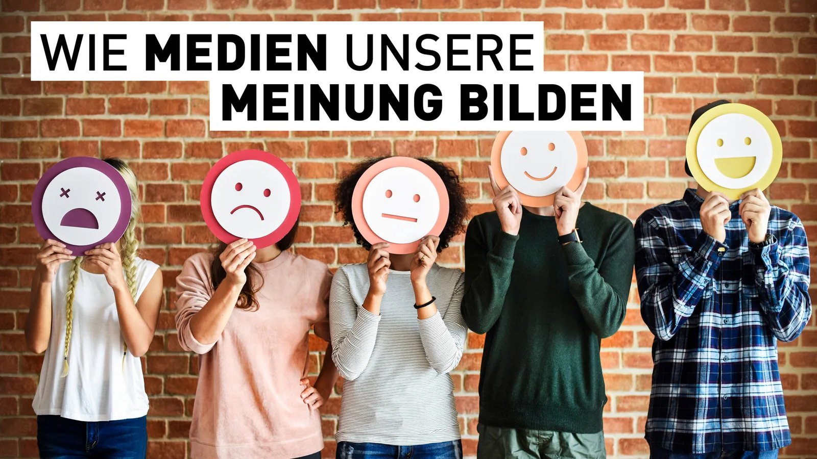 Fünf Personen halten bunte Gesichtsmasken mit verschiedenen Emotionen vor Backsteinwand