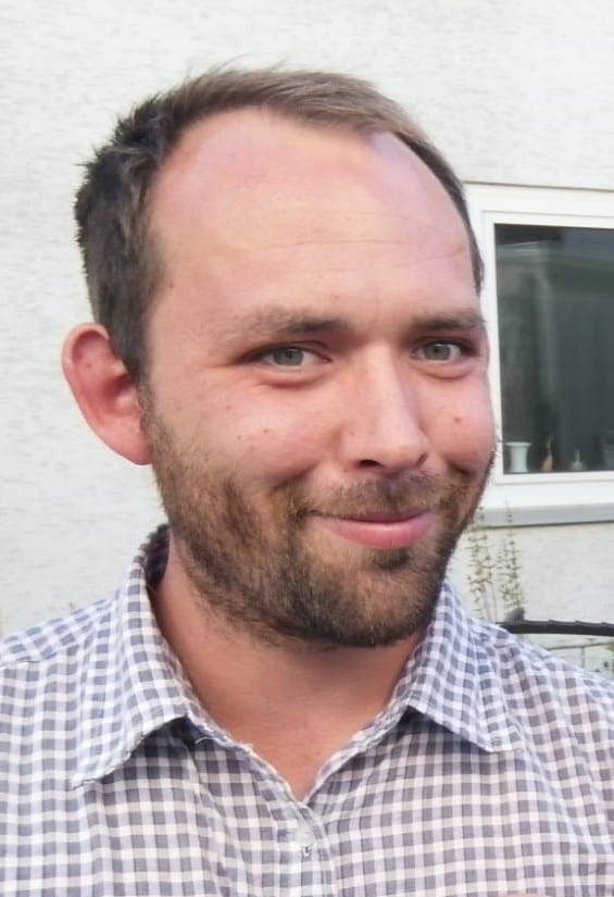 Portrait eines bärtigen Mannes mittleren Alters in kariertem Hemd vor weißer Wand