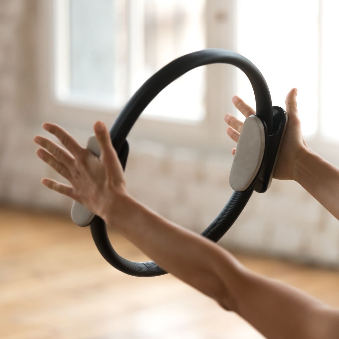 Frau hält schwarzen Pilates Magic Circle mit beiden Händen vor sich