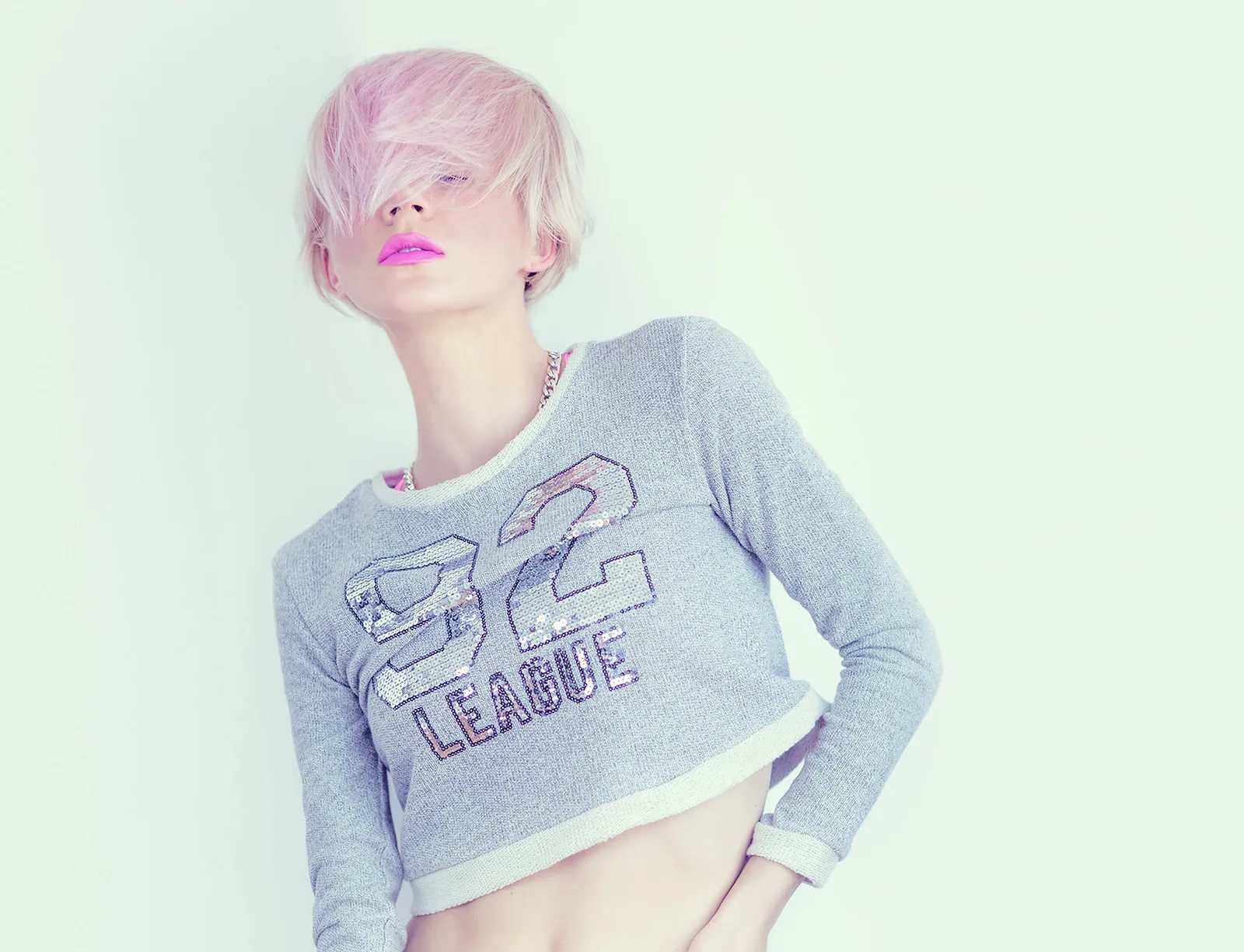 Porträt einer Frau mit pastellrosafarbenem Haar, pinken Lippen, grauem Crop-Top mit violettem Schriftzug, minimalistische Stu