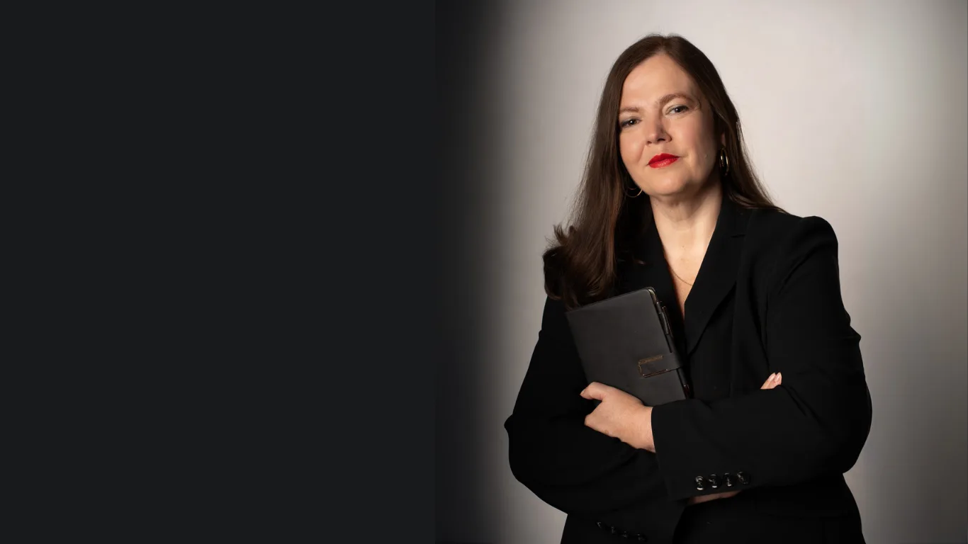 Petra Binder in schwarzem Blazer mit Mappe vor neutralem Hintergrund