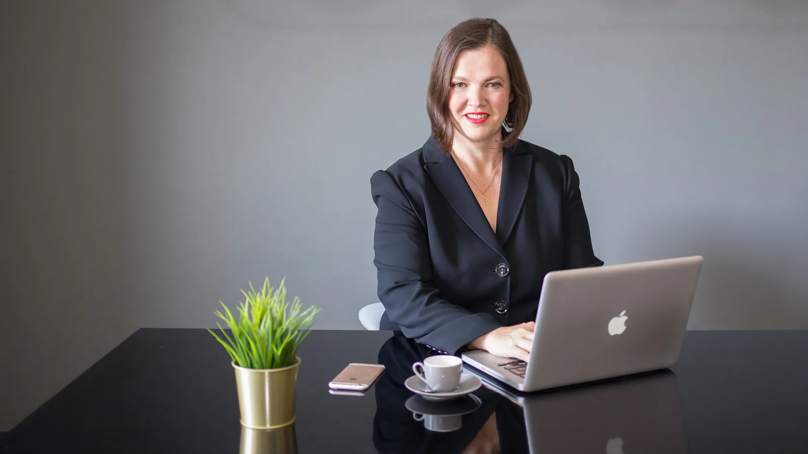 Petra Binder am Schreibtisch mit Laptop, Pflanze und Kaffeetasse – Excellence Strategy Hero-Bild