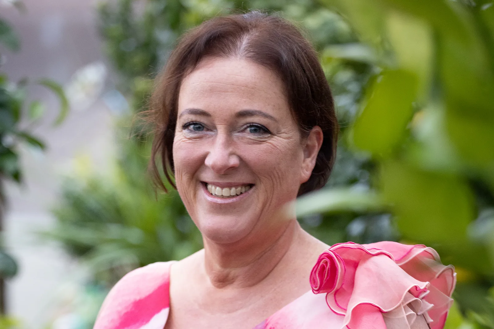 Barbara Tausch lächelnd im grünen Garten, rosa Oberteil mit Rüschen