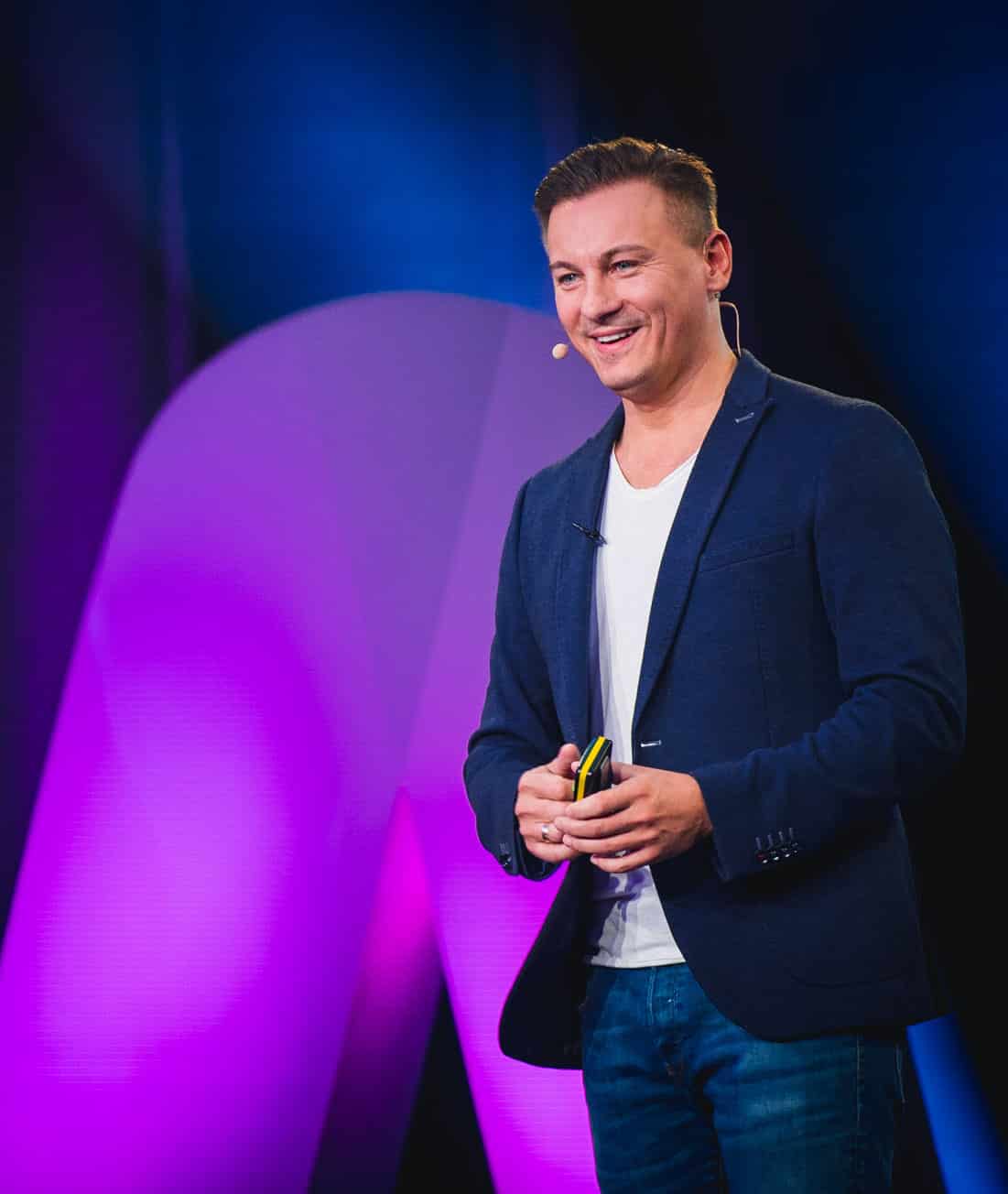 Experten-MasterClass – Webinar zur Leadgewinnung von Dawid Przybylski 4 Mann auf Bühne mit Headset vor blauem und pinkem Hintergrund spricht vor Publikum