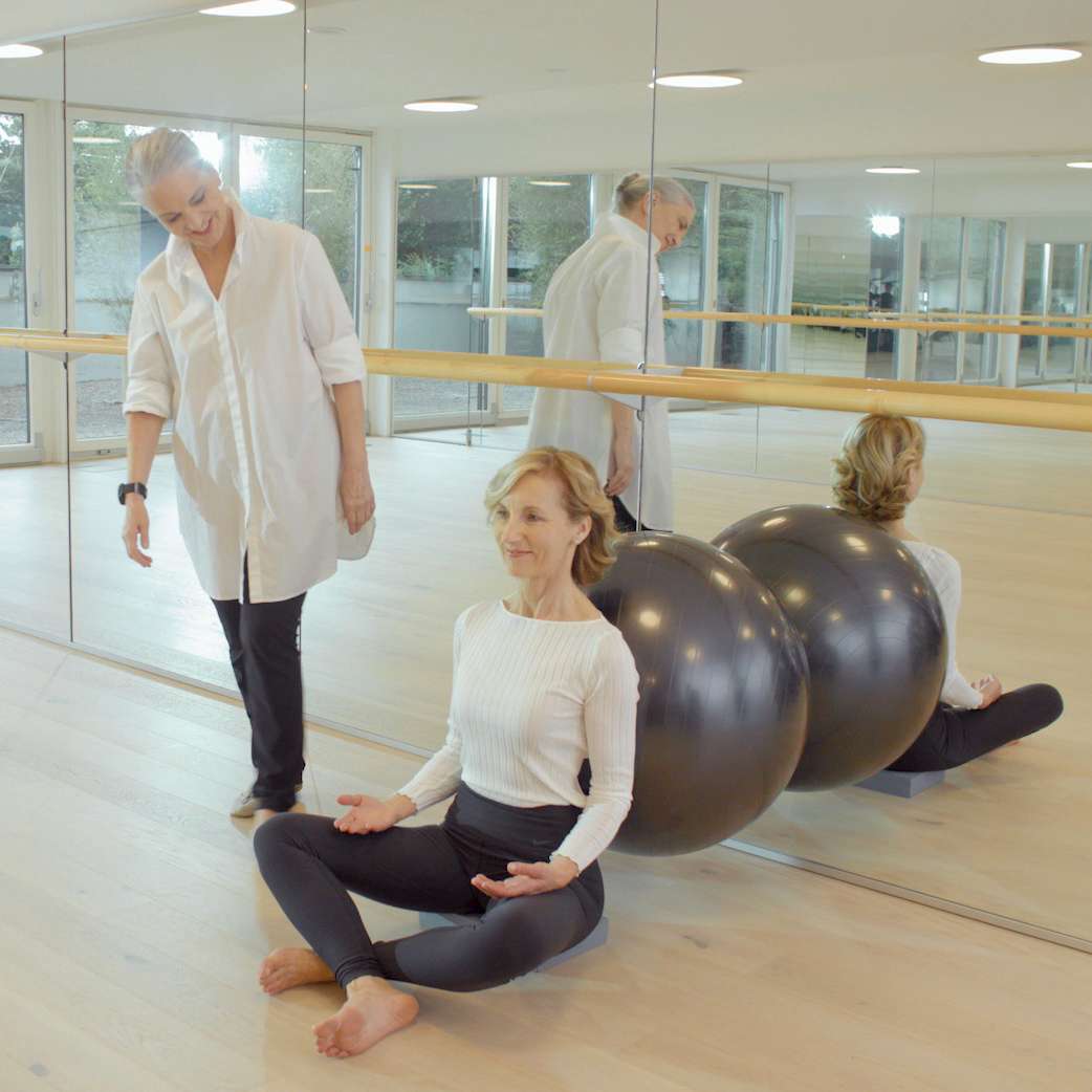Instruktorin begleitet Frau beim Training mit Gymnastikball im Spiegel-Studio