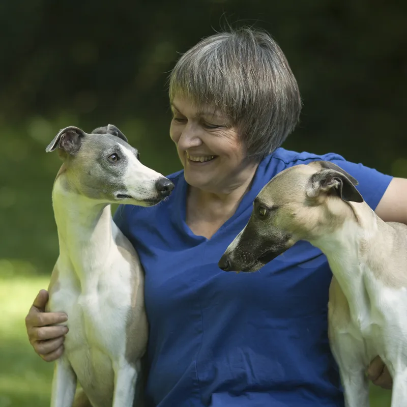 Fallbesprechung: Der unruhige Hund – Webinar zu unruhigen Hunden 1 Eva mit zwei Whippets im blauen Shirt im grünen Freien, lächelnd