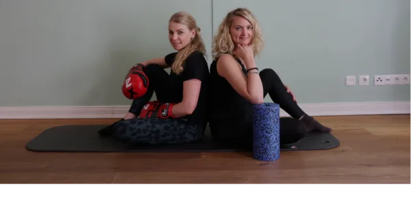 Natalie Zimmermann und Nasrin Schneider Rücken an Rücken auf Trainingsmatte mit Foam Roller