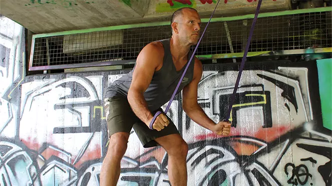 Mann in Trainingskleidung mit Suspensions-Trainer vor Graffiti-Wand, Fitnesstraining mit TRX