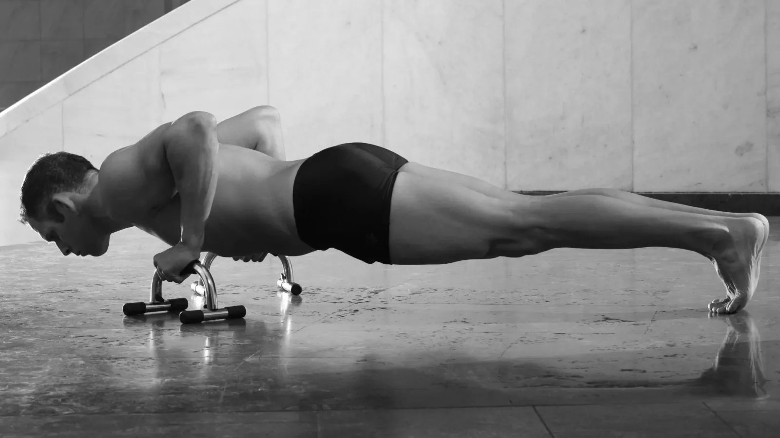 Schwarzweißfoto eines Mannes in Plank-Position mit Hanteln auf Betonboden