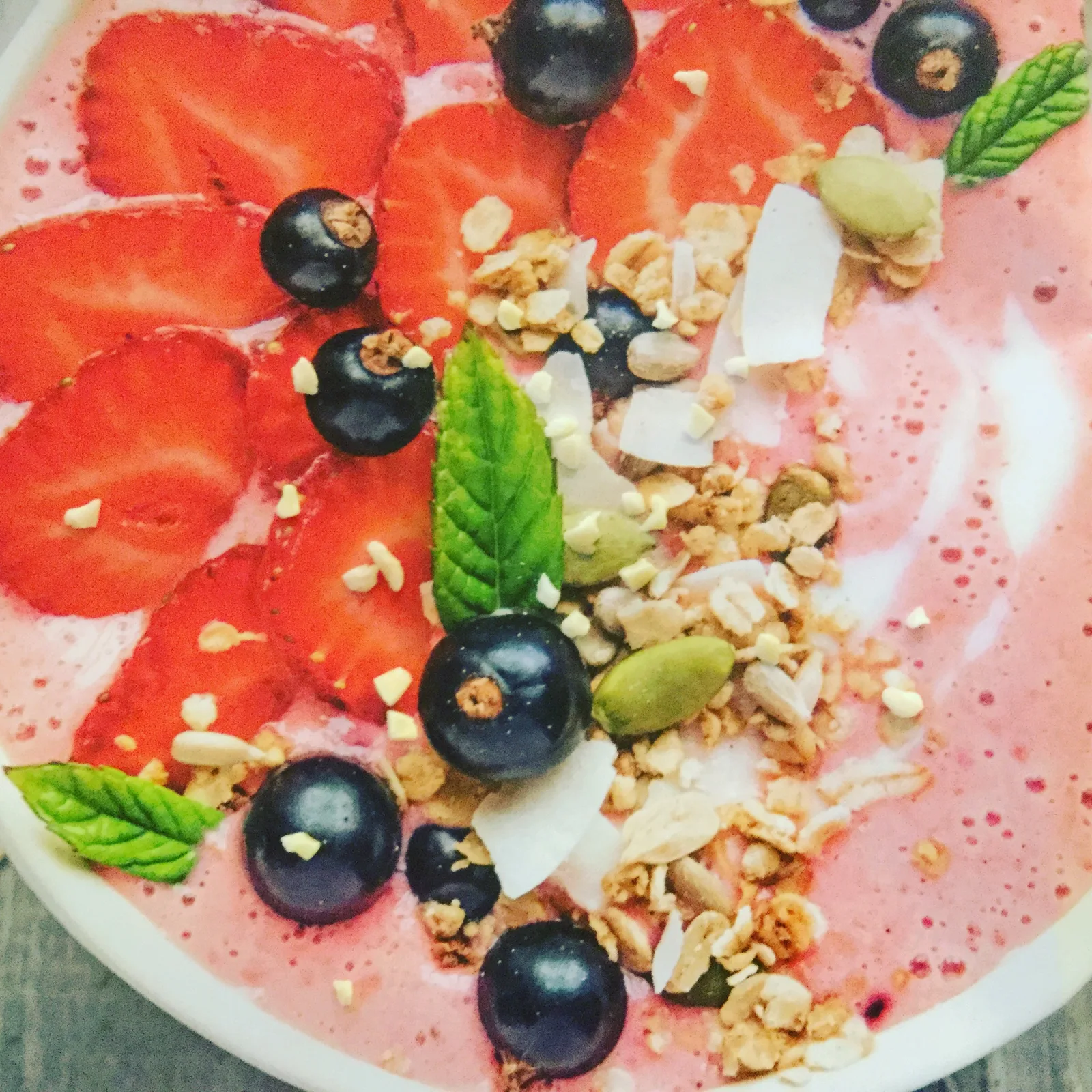 Rosa Smoothie mit Erdbeeren, schwarzen Beeren, Granola und Kokos, dekorativ arrangiert