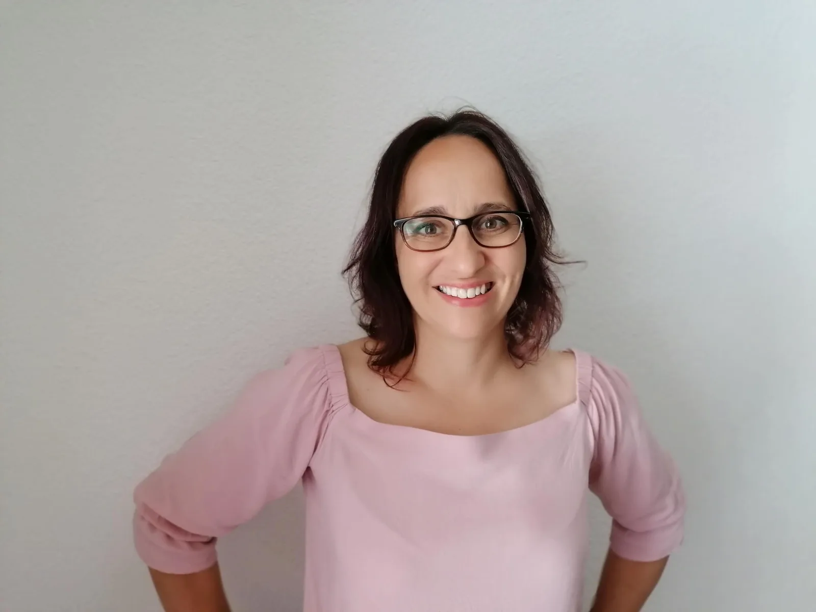 Junge Frau mit Brille, schulterlangen Haaren, rosa Shirt, selbstbewusst lächelnd