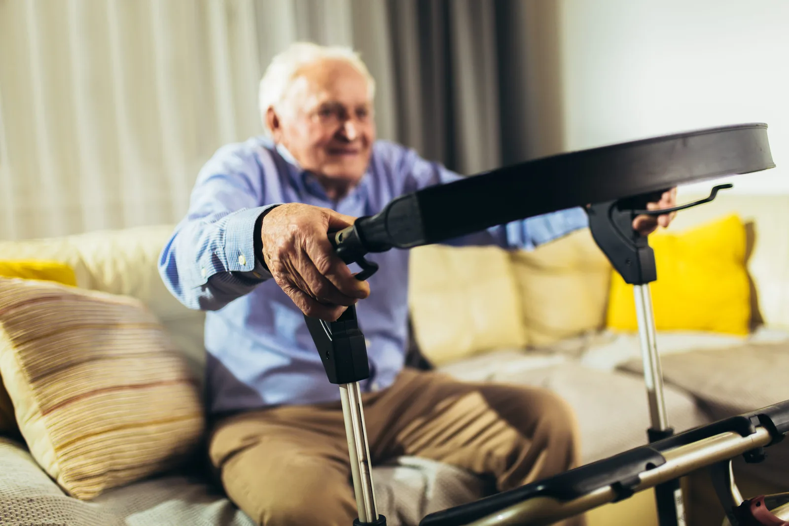 Älterer Mann in blauem Hemd führt Übung mit schwarzem Trainingsband zu Hause auf beigem Sofa durch