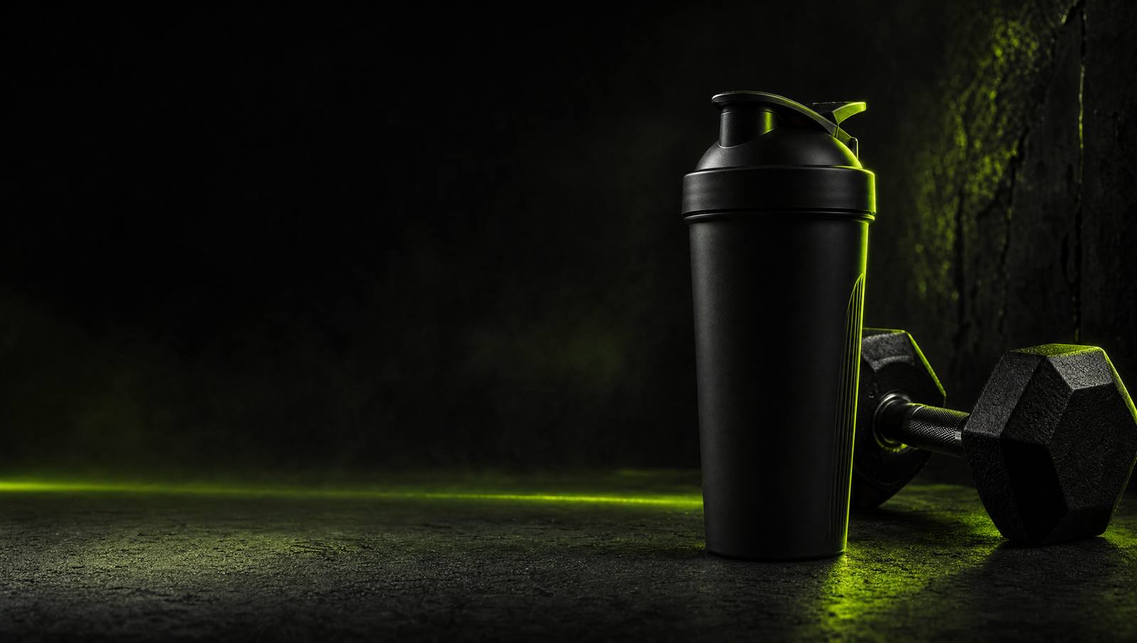 Fitness-Equipment mit schwarzer Trinkflasche und Hantel vor dunklem Hintergrund mit grüner Neon-Beleuchtung