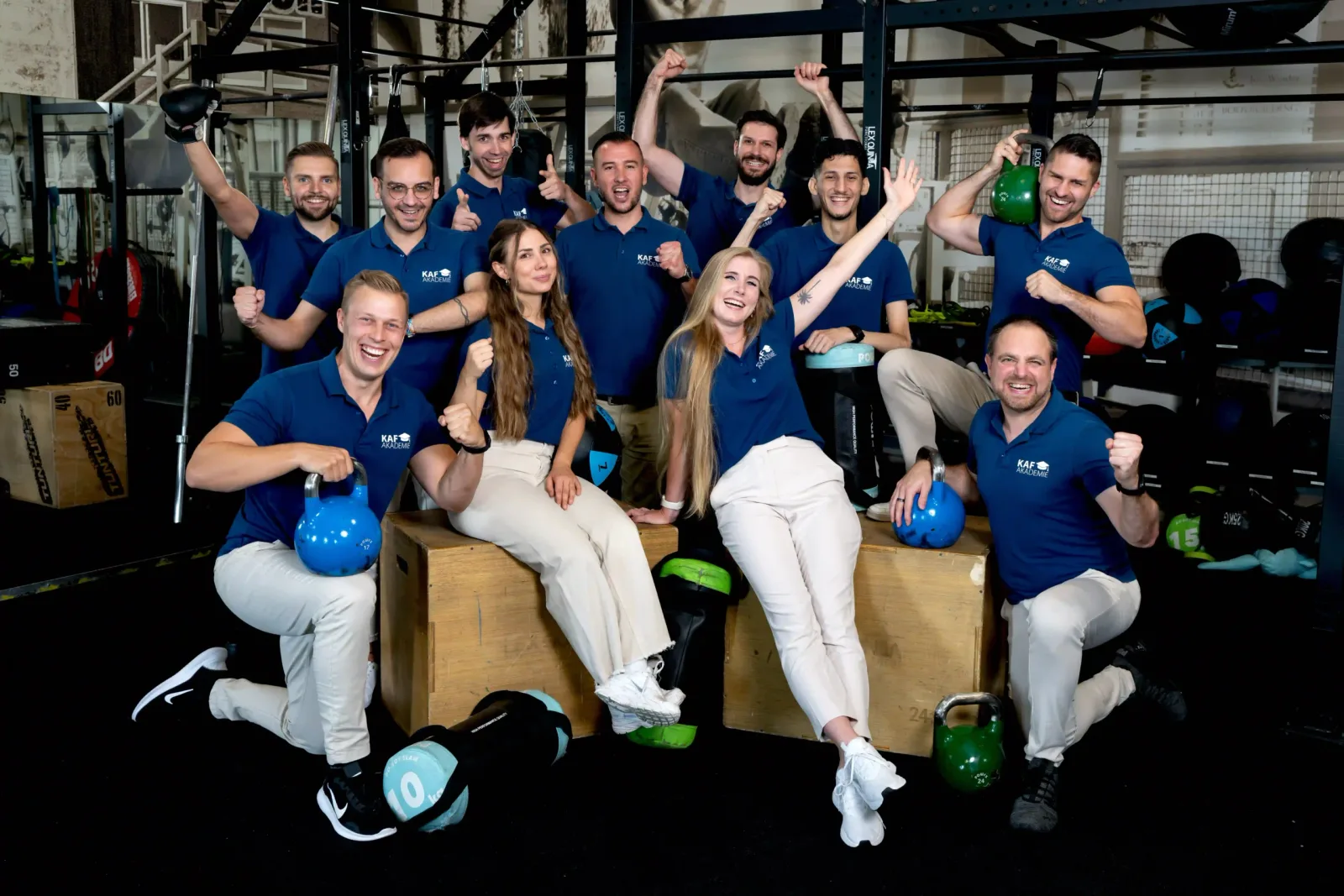 Teamfoto von 13 Personen in blauem KAF Akademie Shirt in Fitnessstudio, fröhliche Pose mit Kettlebells
