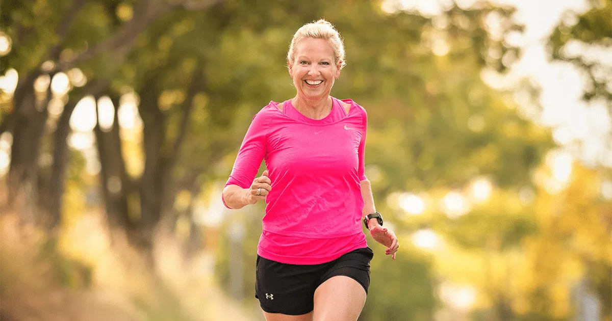 Béatrice Drach joggt lächelnd in pinkfarbenem Shirt auf Waldweg