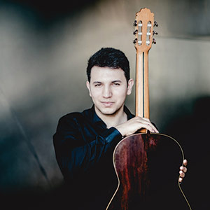 Porträt Kian Soofizadeh mit Klassikgitarre vor grauem Hintergrund