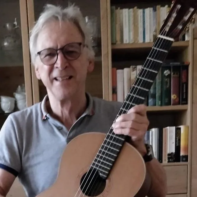 Älterer Gitarrist mit weißen Haaren und Brille hält Klassikgitarre