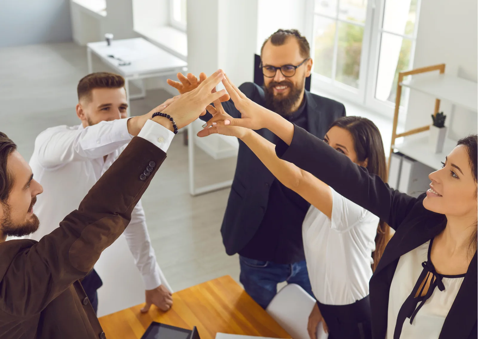 Gruppe von fünf Personen macht High-Five-Geste in modernem Büro, Teamwork und Erfolg