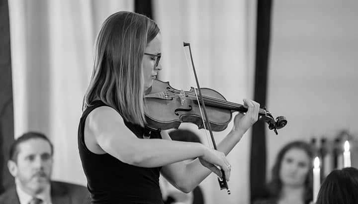 Frau mit Brille spielt Violine auf einer Bühne vor sitzendem Publikum